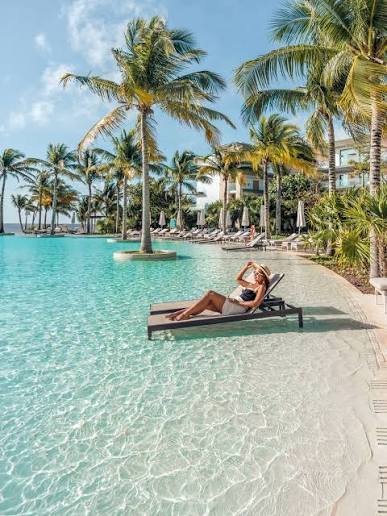 A traveler relaxing on a poolside lounger surrounded by palm trees at an all-inclusive resort
